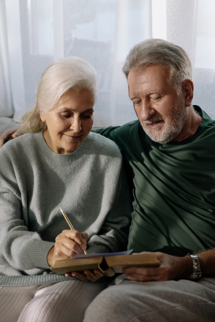 An affectionate elderly couple writing in a notebook while sitting together indoors.