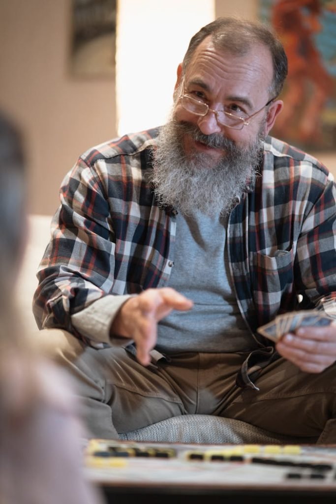 Senior man with a beard and glasses enjoys playing board games indoors. Cozy home environment.